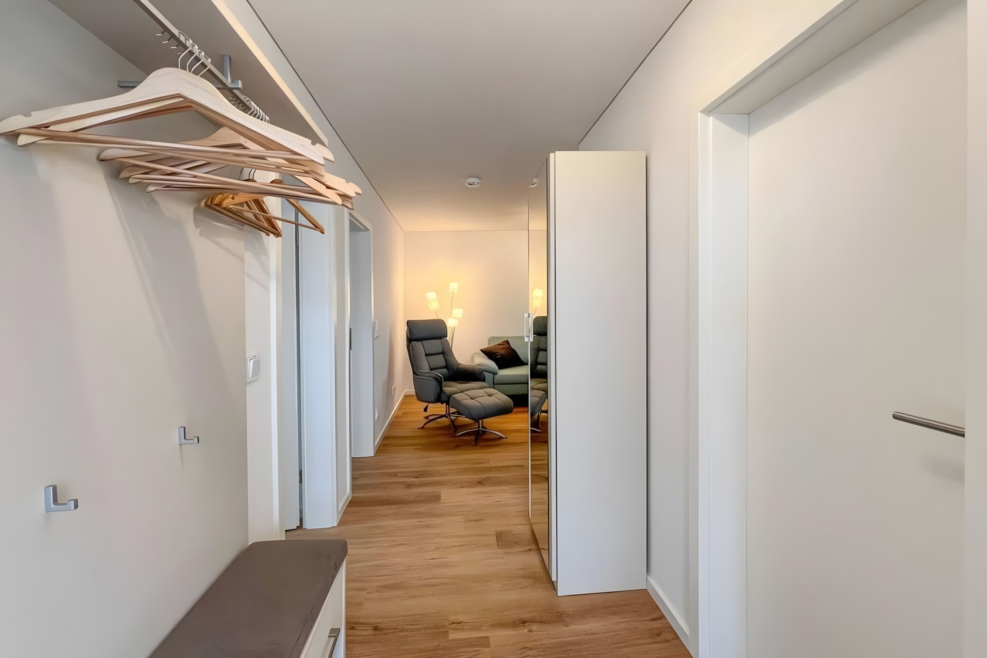Ein Flur mit einer Bank, Holzkleiderbügeln, einem Sessel und einem Sofa.