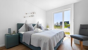 A modern bedroom with a bed, bedside tables, a chair, and a large window. - Holiday Apartment 'Maltes' with Sea View, Private Terrace and Wi-Fi (Kappeln)