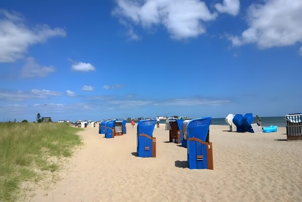 A beach with rows of blue beach huts numbered 9 and 12, a sandy path, and the ocean in the background.