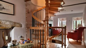 Una escalera de caracol con barandillas de madera, un sillón rojo y una mesa de centro de cristal con diversos objetos.
