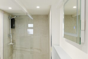 Une salle de bain moderne avec une douche à l’italienne en verre, des carreaux de couleur beige et un grand miroir.