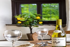 A dining table with a bottle of wine, two empty wine glasses, and a vase with green leaves and yellow flowers. - Cottage in Hawkshaw with Countryside Views (Bury)
