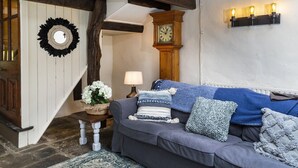 Un salon chaleureux avec un canapé gris, une horloge en bois et un luminaire fixé au mur.