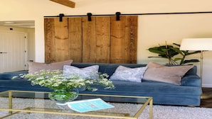 A living room with a blue sofa, a glass coffee table, and a wooden wall panel.