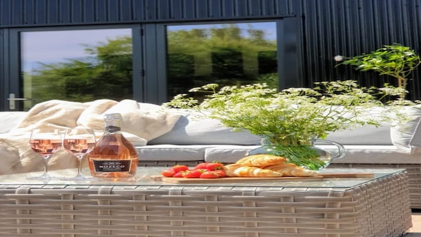A glass table with a bottle of rosé wine, two glasses, a plate of strawberries, and croissants.