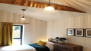 A bedroom with a bed, a dresser, a window with curtains, a hanging light fixture, and framed pictures on the wall.