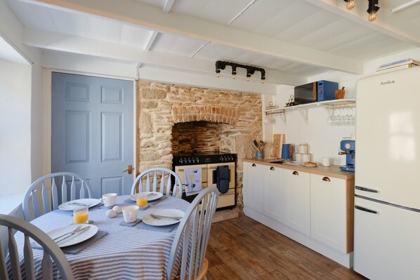 A cozy kitchen with a stone fireplace, white cabinets, and a dining table set for breakfast.