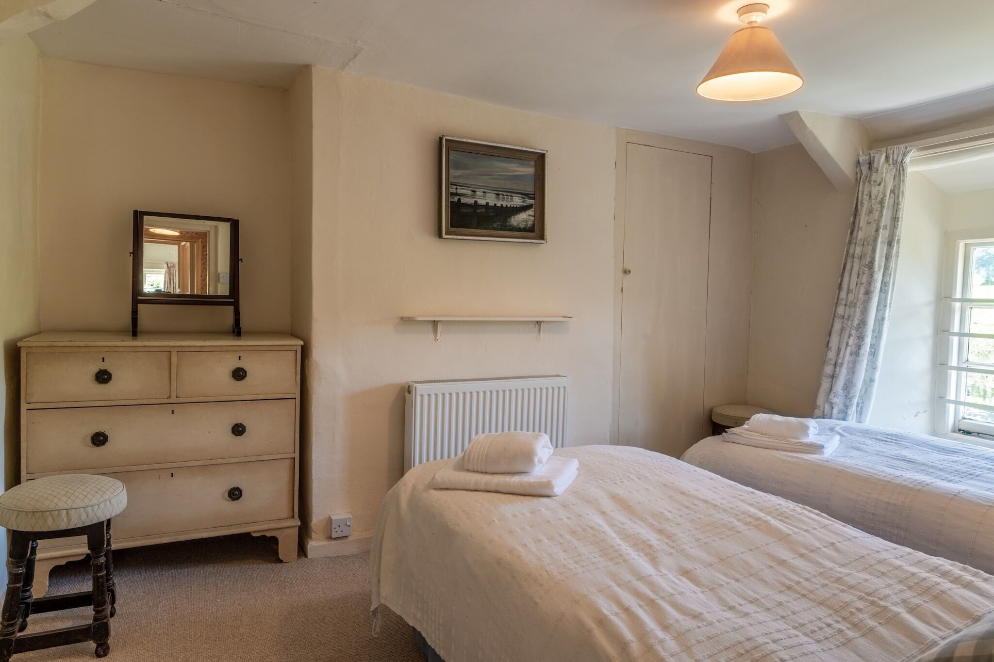 A bedroom with two beds, a dresser, a radiator, and a window with curtains.