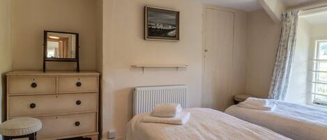 A bedroom with two beds, a dresser, a radiator, and a window with curtains.