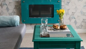 Ein türkisfarbener Couchtisch mit einem Glas, einer Vase voller gelber Blumen und einem Brot.