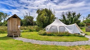 Una cabana de fusta rústica i una tenda blanca en una zona verda, amb arbres al fons.