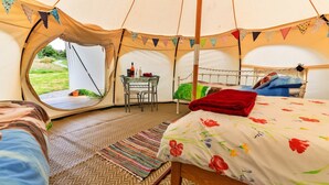 A tent with a bed, a table with chairs, and a view of the outdoors. - Bell Tent in Devon with Countryside Views (Ilfracombe)