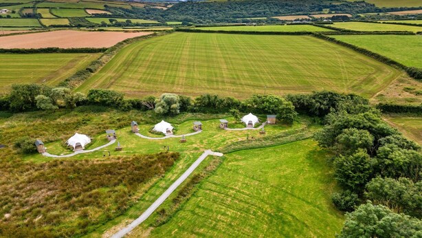 An aerial view of a rural property with several white cottages, a winding path, and expansive green fields. - Bell Tent in Devon with Countryside Views (Ilfracombe)