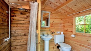Baño de cabaña de madera con ducha, lavamanos, inodoro y ventana.