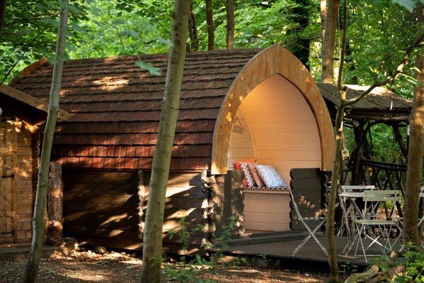 Une cabane en bois rustique, dotée d’un toit en pente, d’un petit porche avec des chaises pliantes et d’un banc à l’intérieur.