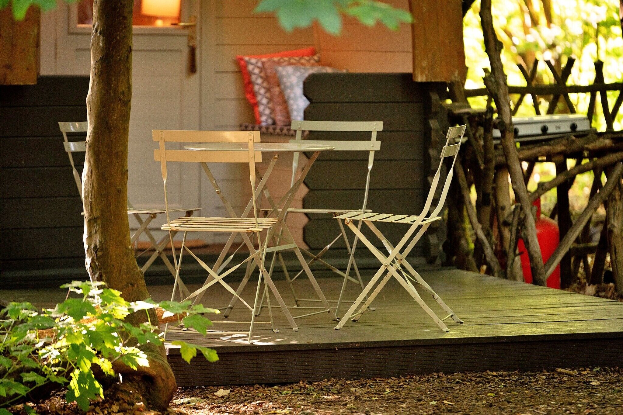 A wooden deck with a table and chairs, surrounded by a wooden fence and a tree.