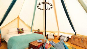 L’intérieur d’une tente accueillante, avec un lit, des oreillers, une petite table et un panier.