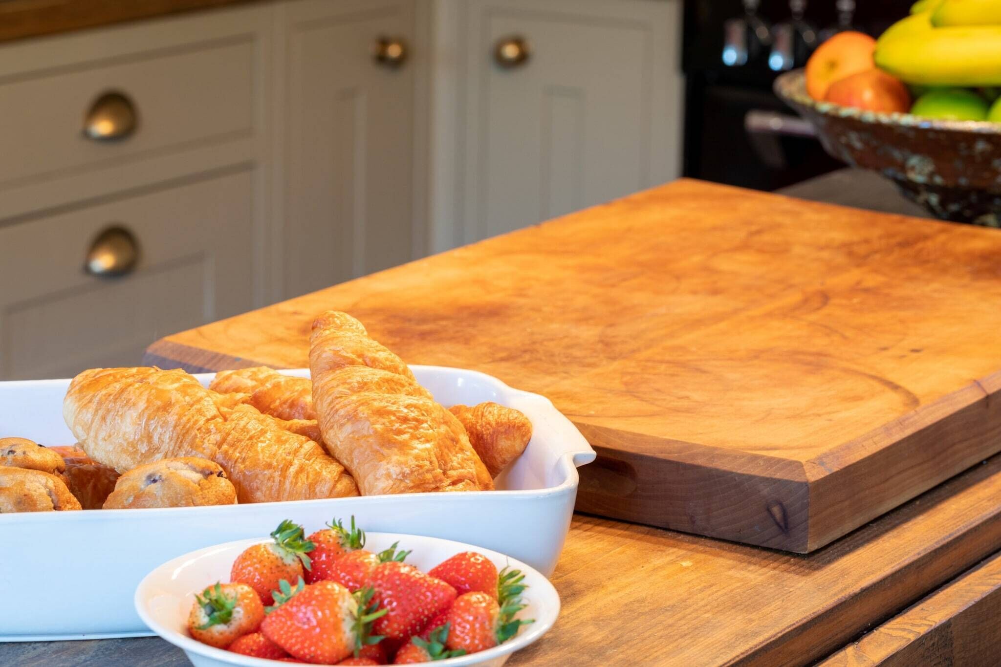 A kitchen counter with a bowl of croissants and a bowl of strawberries.