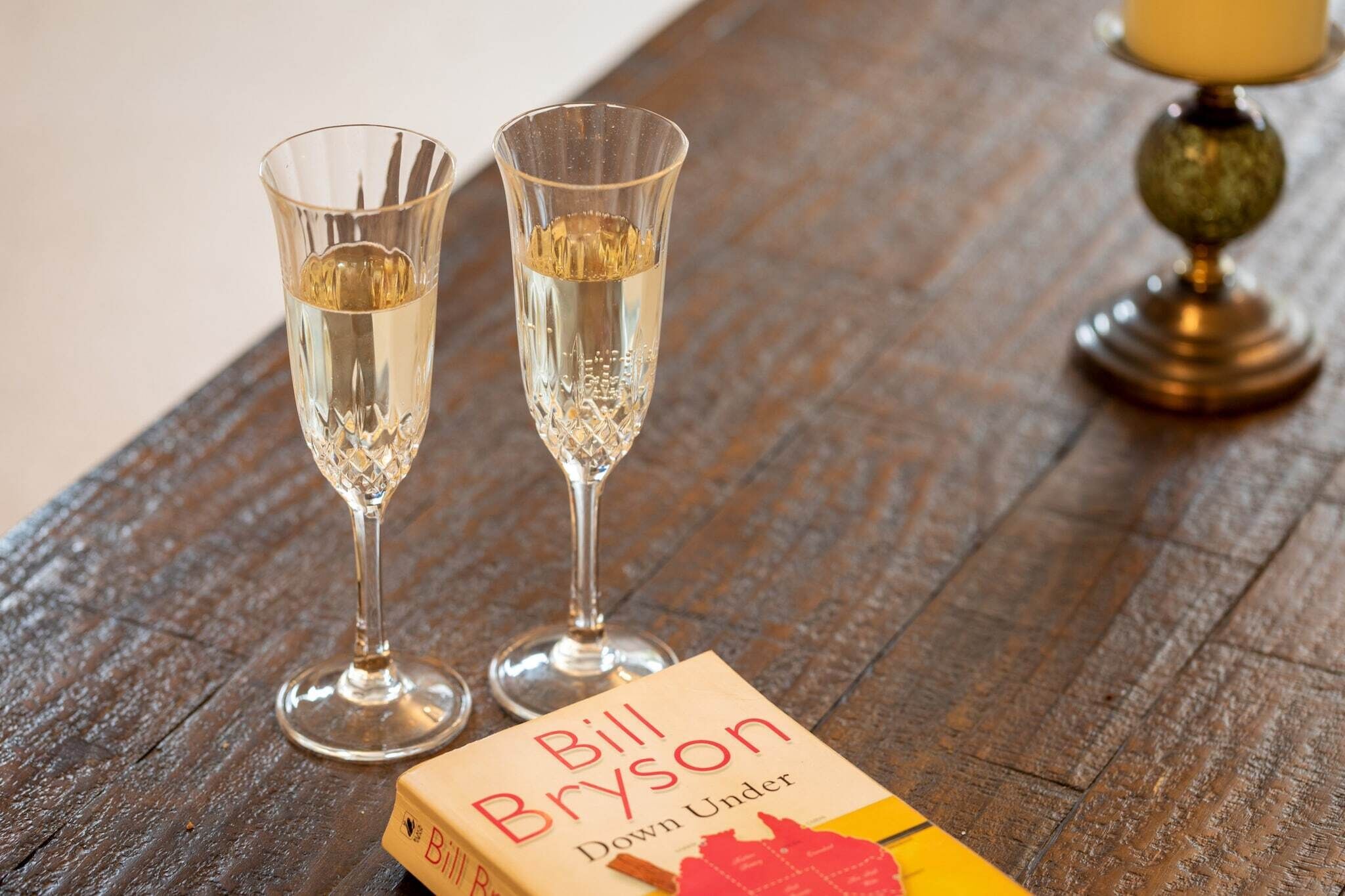 Deux flûtes à champagne sont posées sur une table en bois, à côté d’un livre intitulé « Down Under » de Bill Bryson.