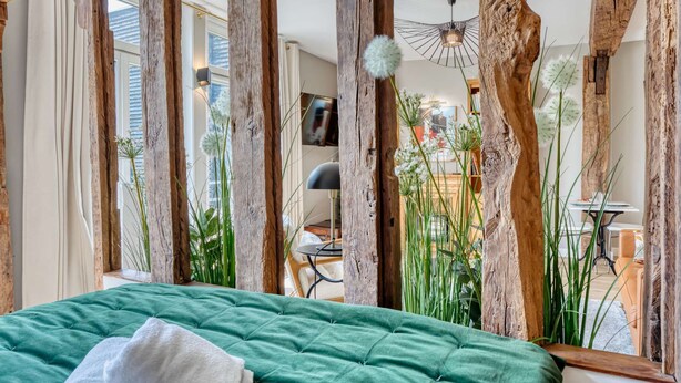 Ein Zimmer mit einem grünen Bett, Holzbalken, einer Hängeleuchte und Zimmerpflanzen.