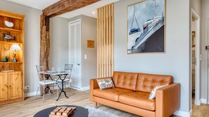Ein Wohnzimmer mit einer Ledersofa, einem Esstisch mit Stühlen, einer Holzkommode und einem Gemälde eines Schiffes.