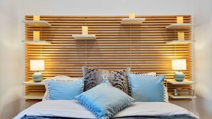 Une chambre à coucher bien rangée, avec une tête de lit en bois à lattes, deux tables de chevet avec des lampes et un lit recouvert d’une literie bleue.