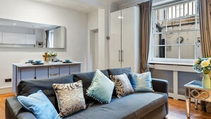 Un salon moderne avec un canapé gris, une petite table d’appoint et une fenêtre avec des rideaux.