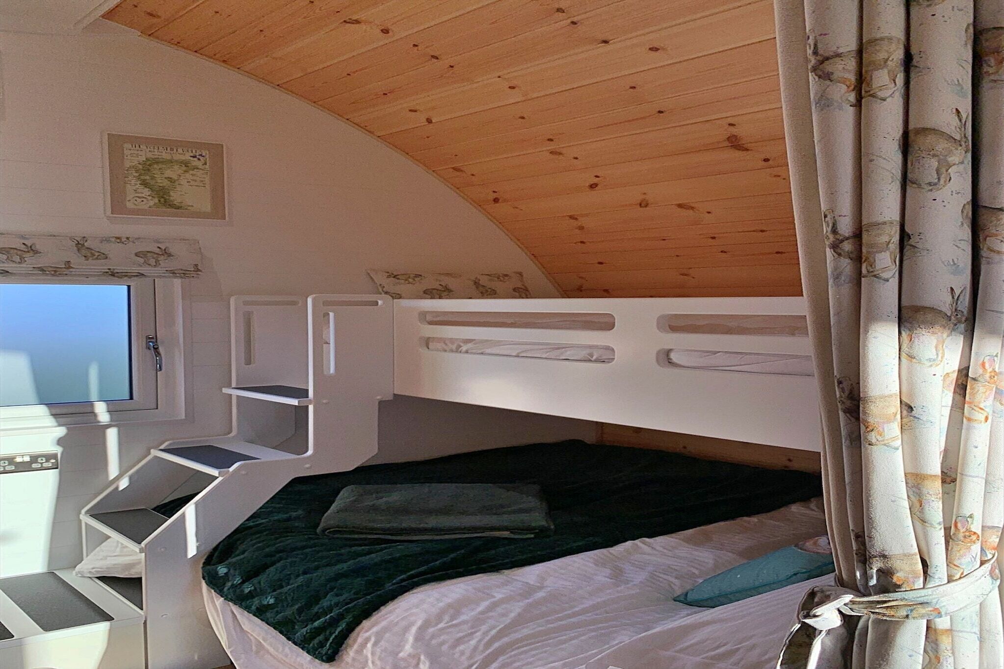 A bunk bed with a TV on a desk, a map on the wall, and a window with curtains.