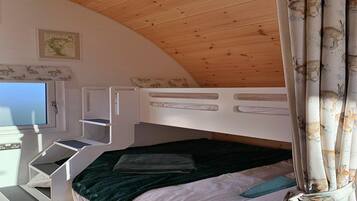 A bunk bed with a TV on a desk, a map on the wall, and a window with curtains.