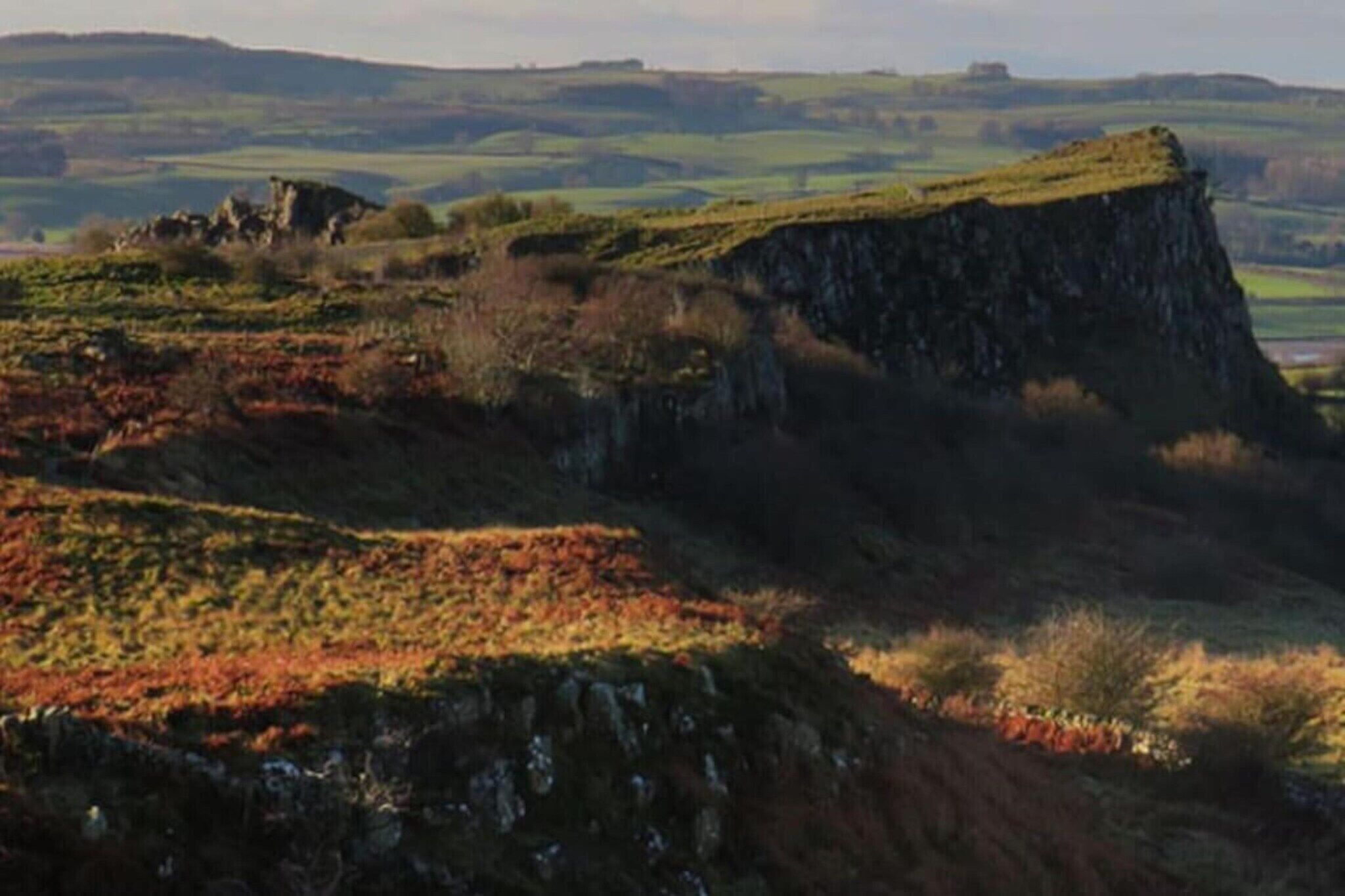 Un paysage caractérisé par une falaise imposante et des collines douces en arrière-plan.