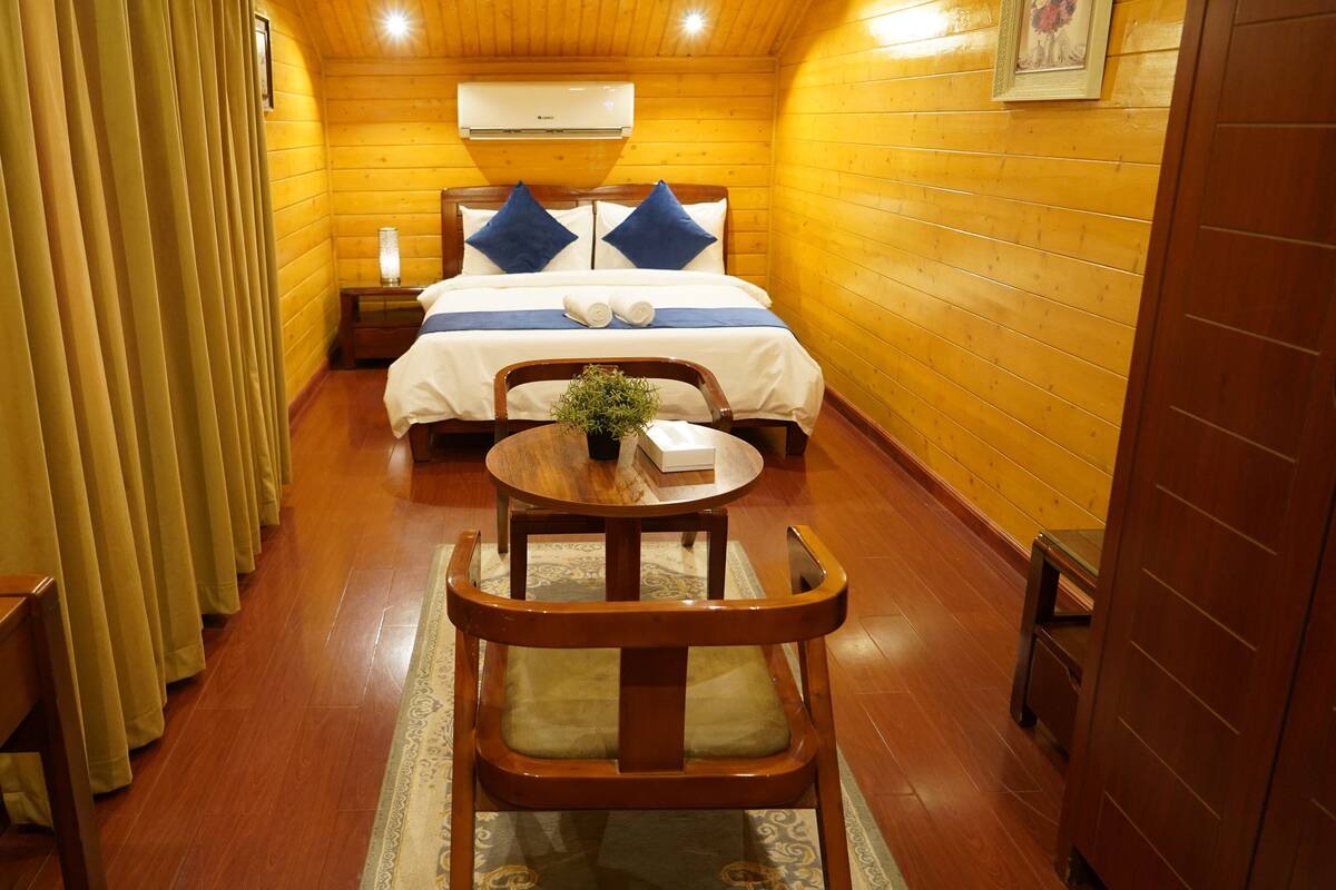 Una habitación cálida de cabaña de madera con una cama, una pequeña mesa con una planta y una silla.