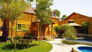 A wooden house with a swimming pool, a covered patio, and a well-maintained lawn. - The Land Villas Ammaria (Diryah)