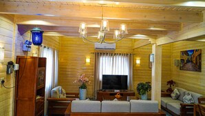 A cozy wooden cabin interior with a wooden bench, a television, a chandelier, and a painting on the wall. - The Land Villas Ammaria (Diryah)