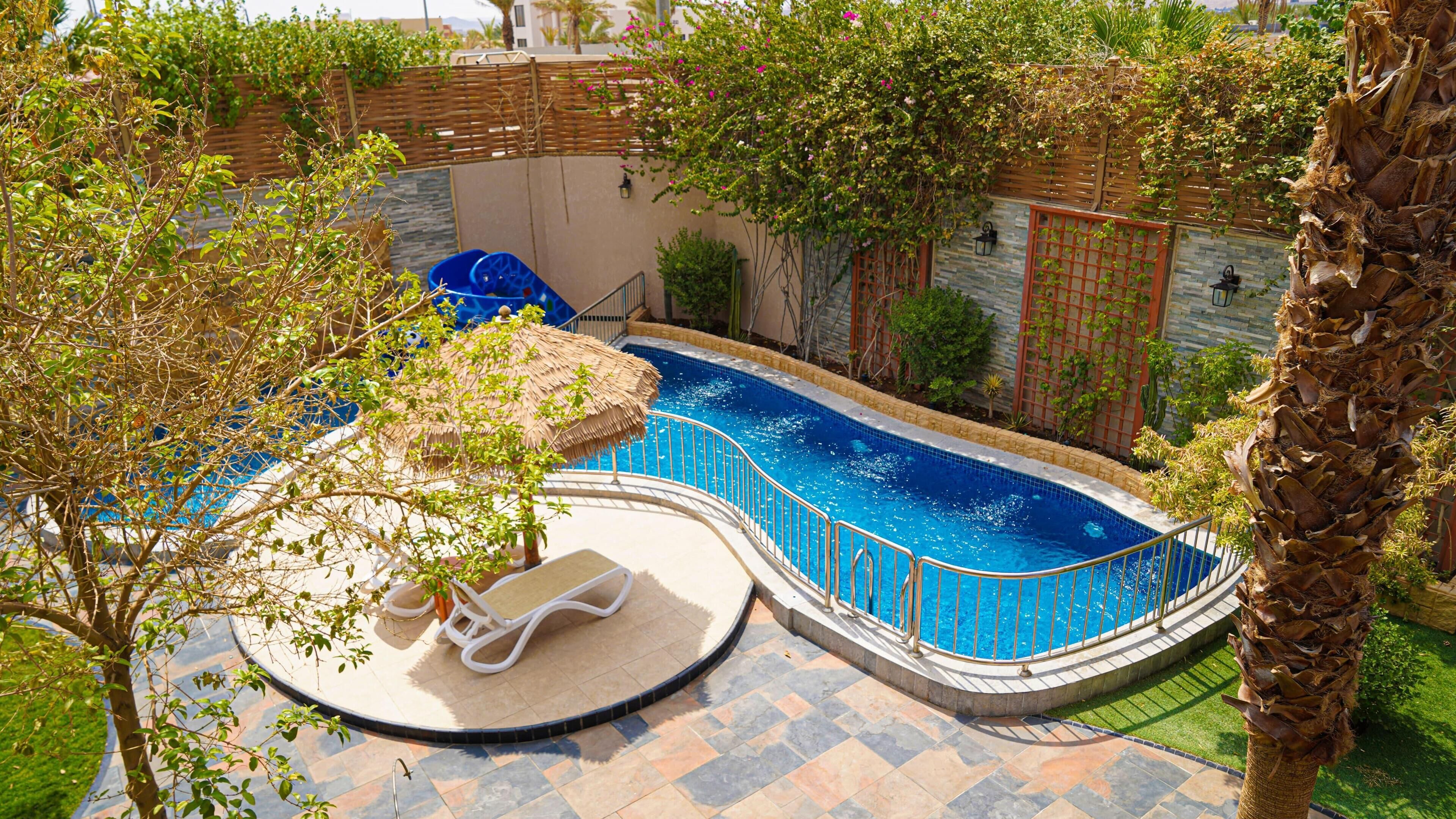 A swimming pool with a curved design, surrounded by a wooden fence and various plants.
