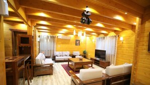 A wooden cabin interior with a sofa, TV, and wooden furniture. - The Land Villas Ammaria (Diryah)