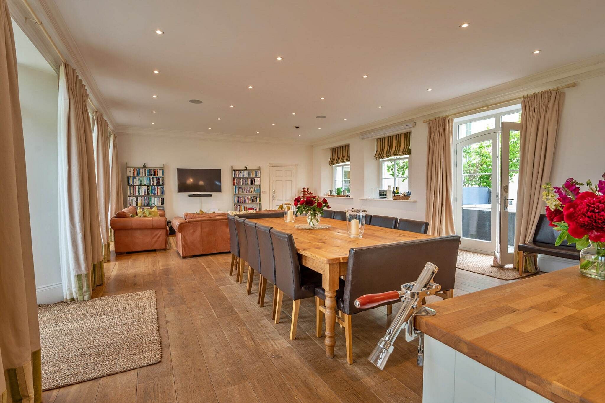 A spacious dining area with a wooden table and chairs, a television, and bookshelves.