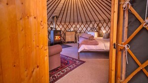 L’intérieur d’une yourte, avec un lit, une petite table, un chauffage et un tapis.