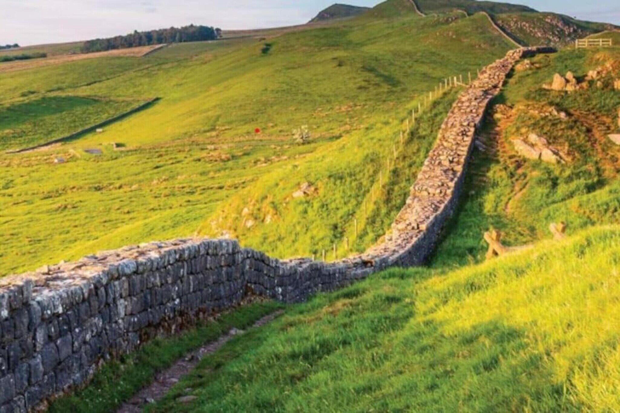 Un muro in pietra serpeggia attraverso un paesaggio erboso sotto un cielo limpido.