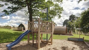A playground with a slide, climbing structure, and a wooden playhouse. - Pet-friendly Lakeside Cabin. (Hexham)