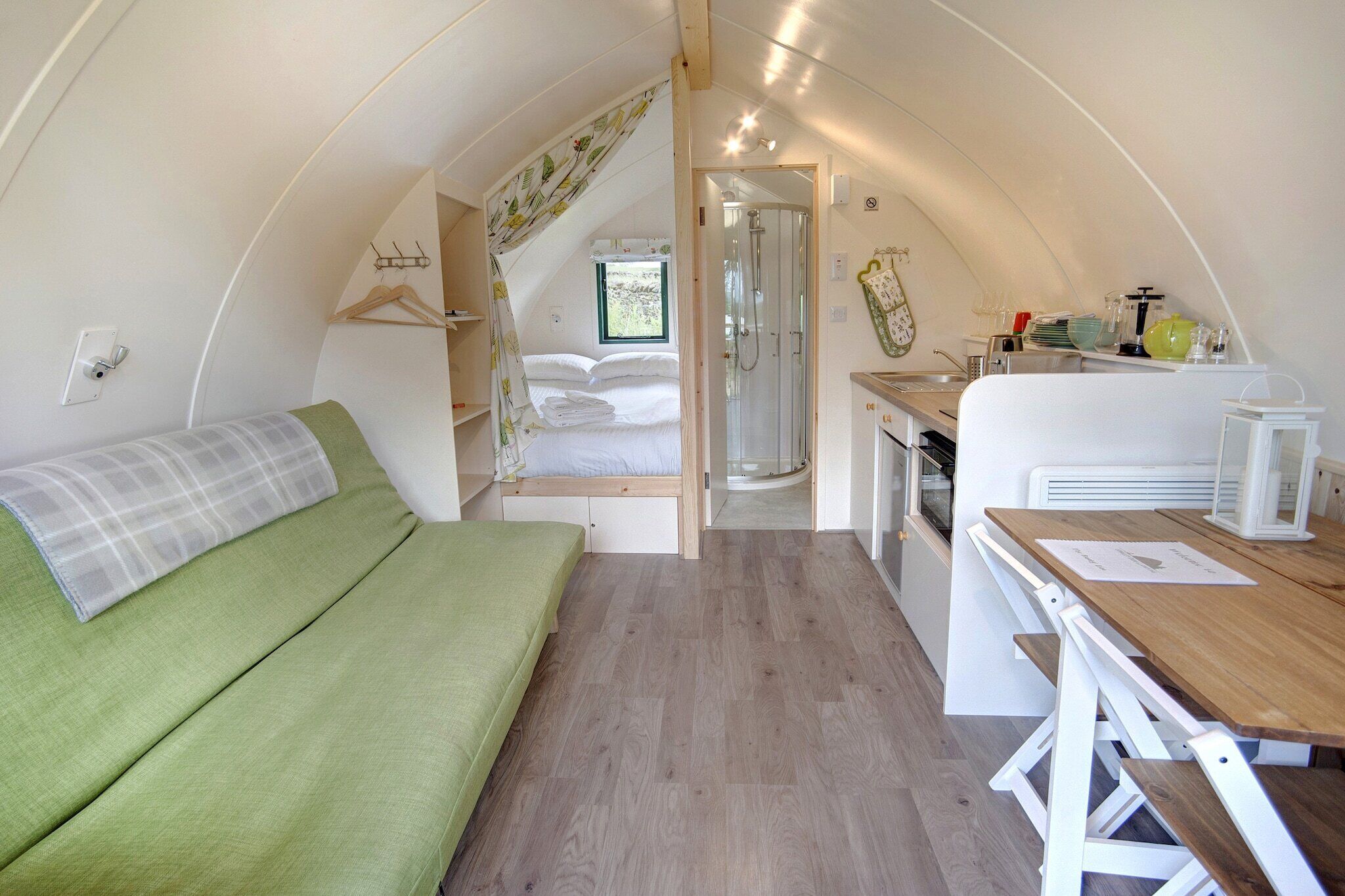 Un interior compacto y bien iluminado con una cama, una pequeña kitchenette y una ducha.