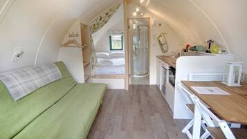 Un interior compacto y bien iluminado con una cama, una pequeña kitchenette y una ducha.