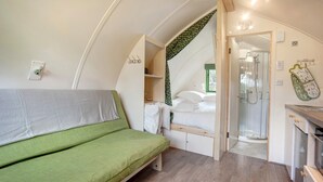 Une pièce compacte avec un canapé vert, un lit avec une literie blanche, une petite kitchenette et un espace douche.