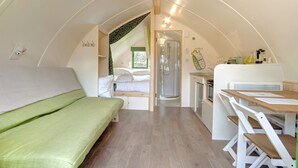 Habitación compacta y bien iluminada con cama, ducha y pequeña kitchenette.
