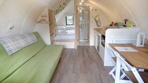 Een compact, goed verlicht interieur met een bed, een kleine kitchenette en een douche.