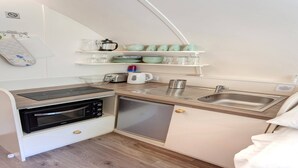 Una kitchenette compacta con horno integrado, microondas y lavavajillas. Hay estantes sobre la encimera con diversos utensilios de cocina y una tetera.