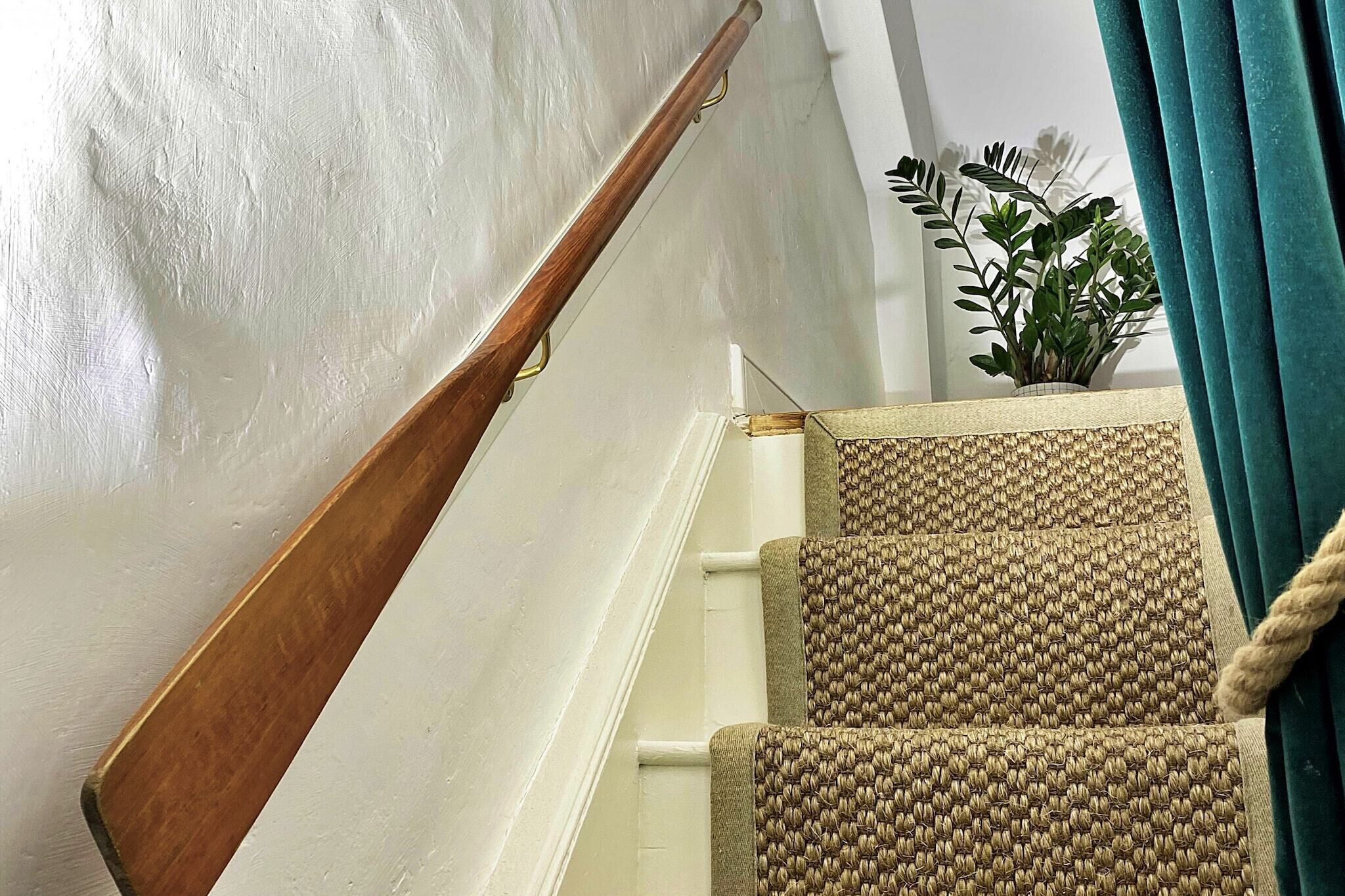 Une main courante en bois sur un escalier dont les marches sont recouvertes d’une moquette à motifs.