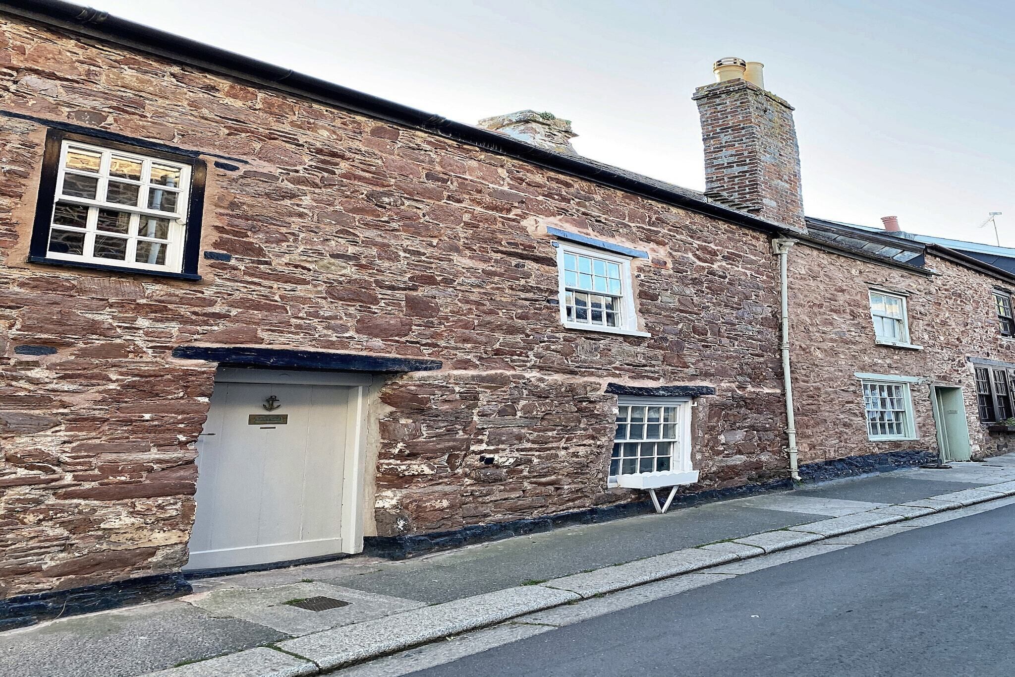 A stone building with multiple windows and doors, a chimney, and a paved sidewalk.