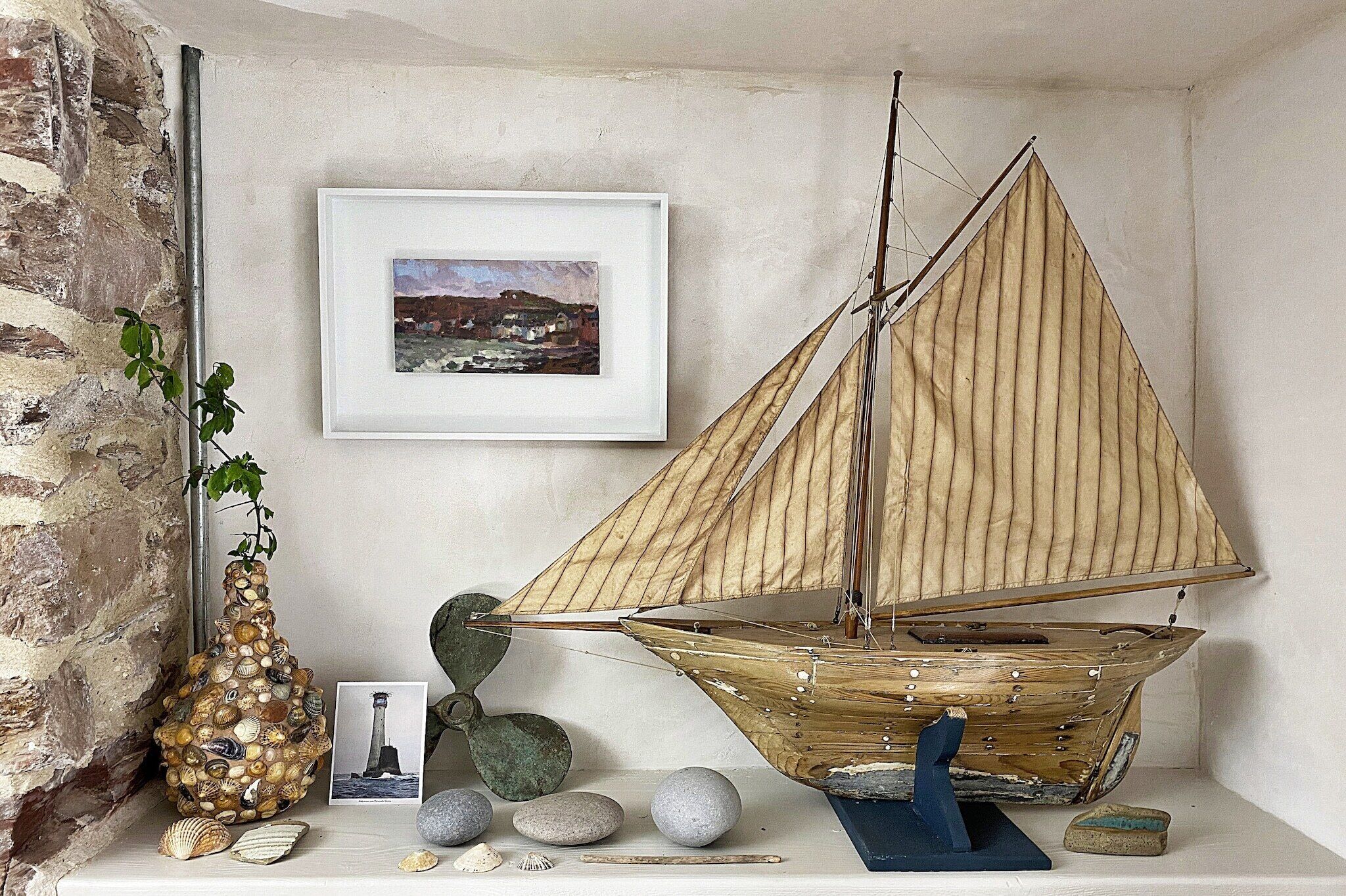 A model sailboat on a shelf, surrounded by seashells and a framed picture.