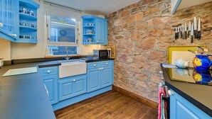 Een keuken met blauwe kastjes, een stenen muur en een raam met jaloezieën.