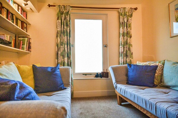 A cozy living room with two sofas, a bookshelf, and a window with curtains. - Cottage in Kingsand with Stunning Sea Views (Kingsand)